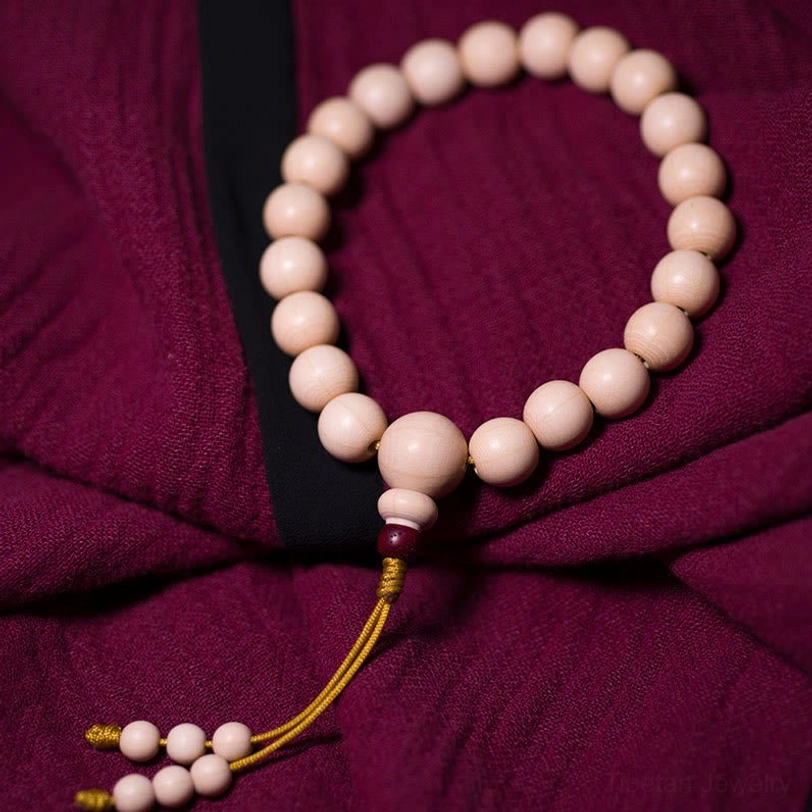 Side profile flat lay of Tibetan wood mala bracelet showing red accent bead placement, yellow woven tassel, and smooth bead arrangement on burgundy background