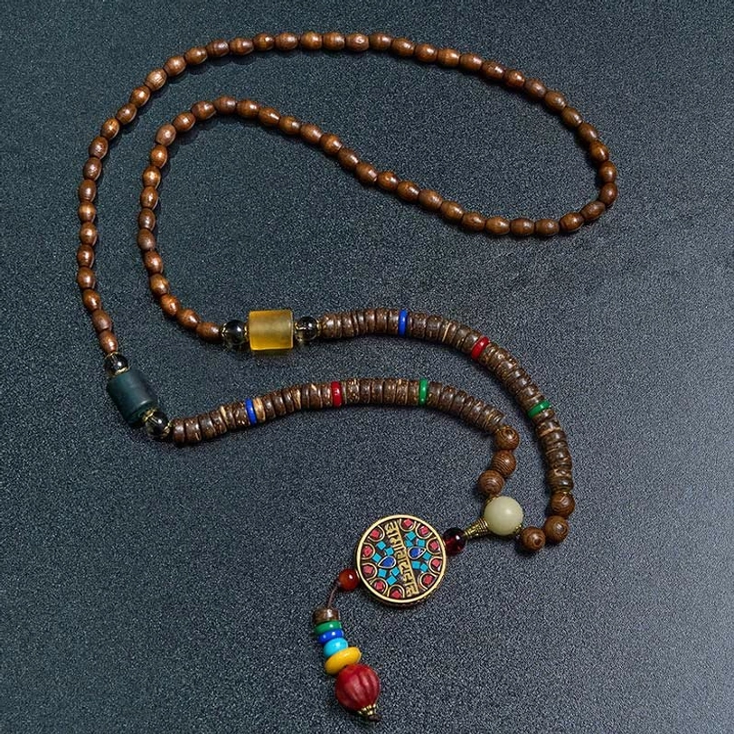 Close-up of Tibetan Buddhist prayer bead necklace with enamel mantra pendant and wooden beads on dark background