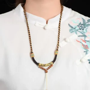 Worn Tibetan prayer necklace with sacred mantra pendant draped around neck on embroidered traditional Buddhist garment