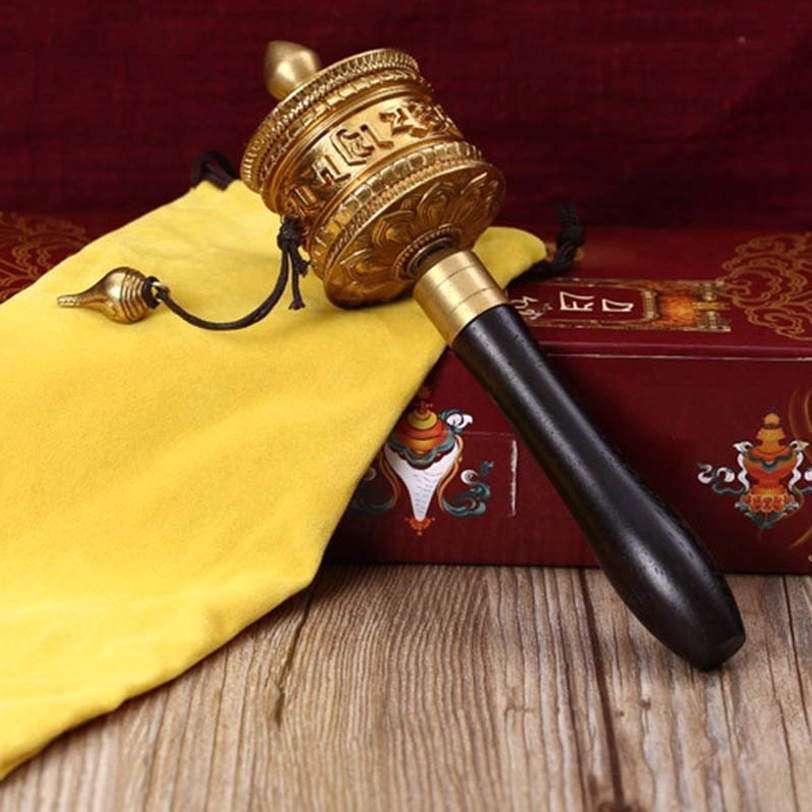 Bronze tibetan prayer wheel with embossed mantras dark wood handle and hanging metal ornament on wooden backdrop