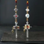 Tibetan prayer wheel car hanging decoration set with silver tone body, colorful gem inlays, endless knot charms, and braided rope on wooden display