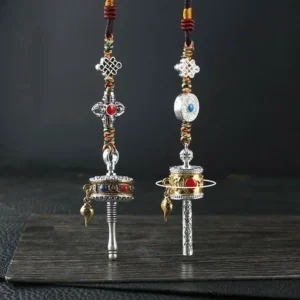 Tibetan prayer wheel car hanging decoration set with silver tone body, colorful gem inlays, endless knot charms, and braided rope on wooden display