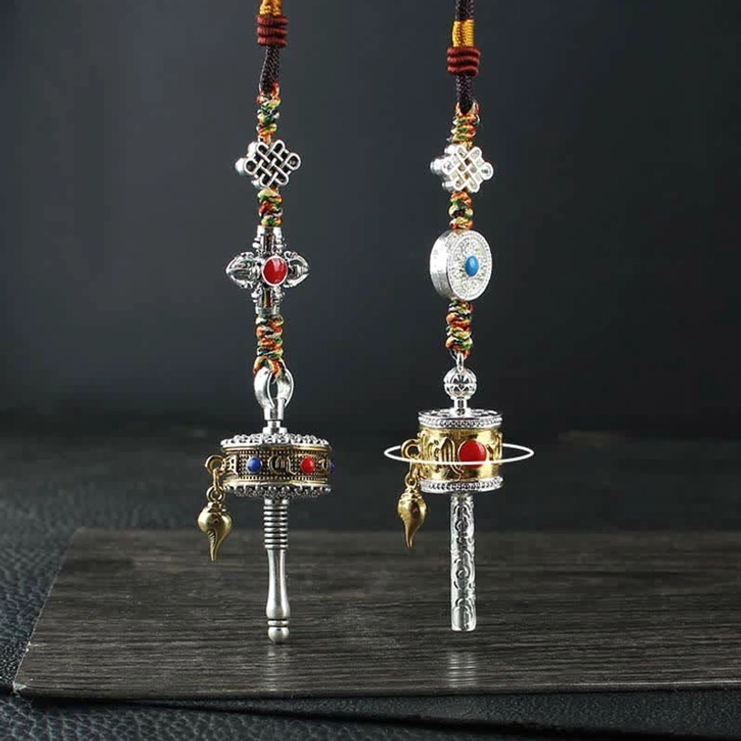 Tibetan prayer wheel car hanging decoration set with silver tone body, colorful gem inlays, endless knot charms, and braided rope on wooden display