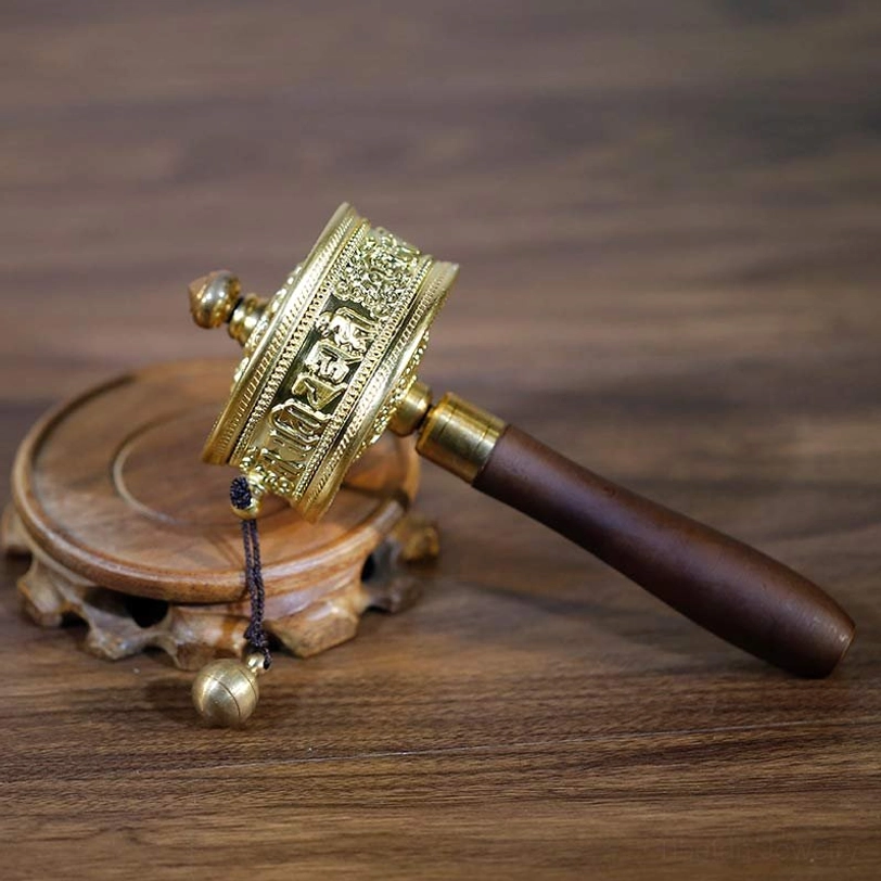 Front end-face view of Tibetan prayer wheel showing brilliant gold tone metal with complex traditional Tibetan floral relief carvings and central decorative knob