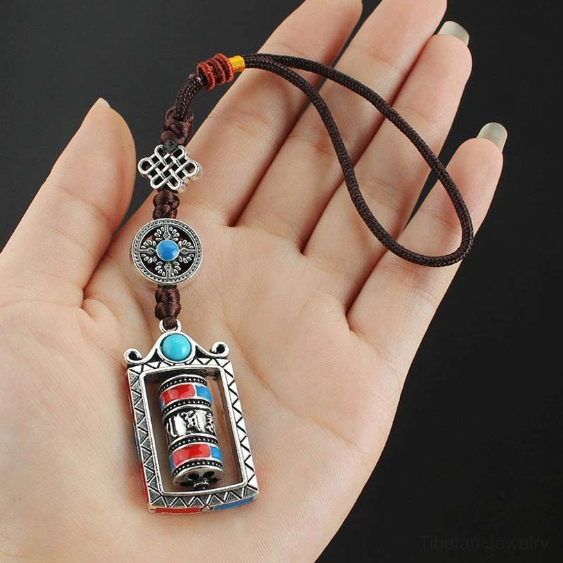 Hand holding Tibetan Om Mani Padme Hum prayer wheel keychain, showing adjustable lanyard and silver alloy construction on palm