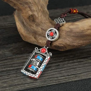 Om Mani Padme Hum prayer wheel keychain with rotatable mechanism, featuring silver alloy, red and blue accents, and dark brown Chinese knot cord on wooden surface