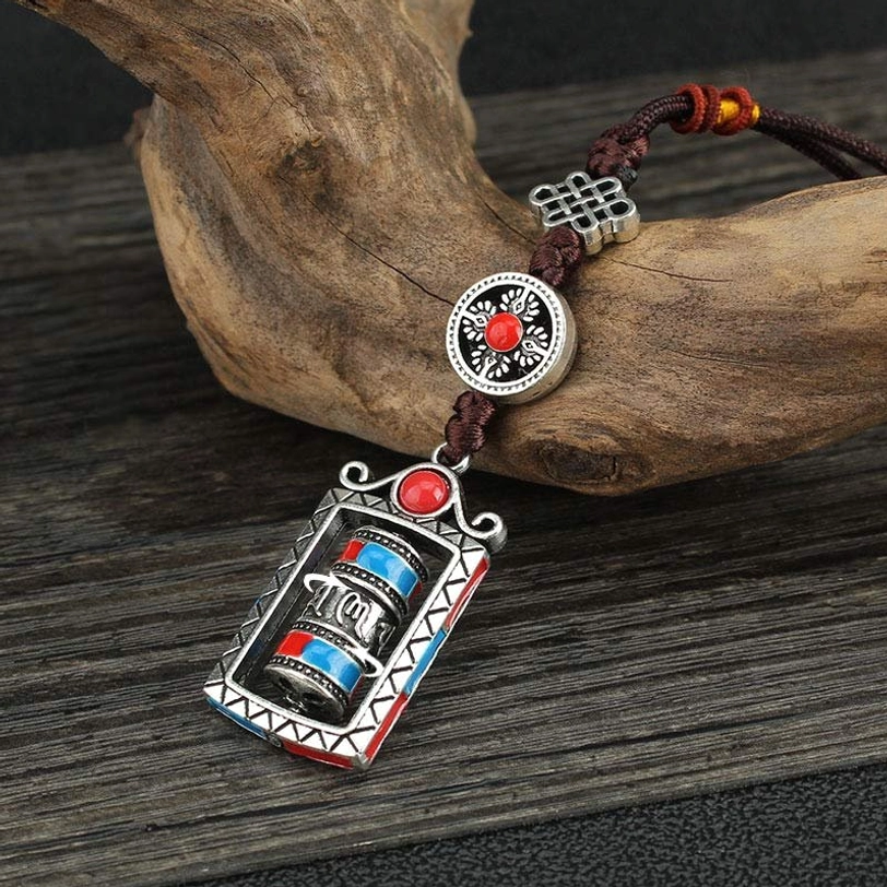 Om Mani Padme Hum prayer wheel keychain with rotatable mechanism, featuring silver alloy, red and blue accents, and dark brown Chinese knot cord on wooden surface