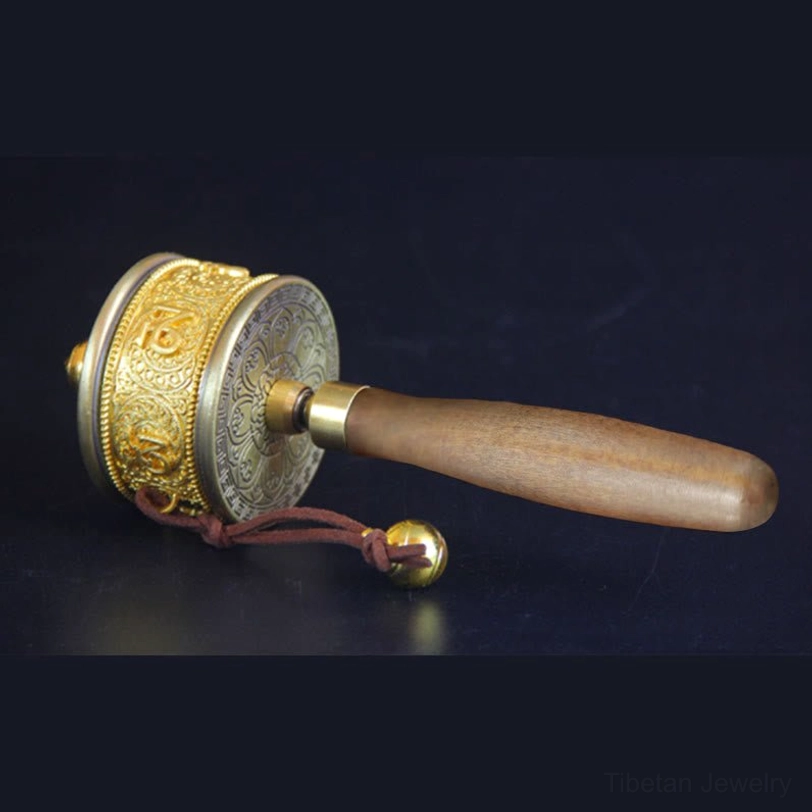 Close-up side view of copper prayer wheel with hand-engraved lotus flower on end cover, sacred Om Mani Padme Hum mantras, and leather hanging cord