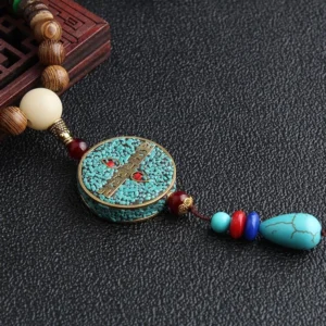 Close-up of Tibetan meditation necklace showing turquoise drop charm and multicolor agate spacer beads on leather surface