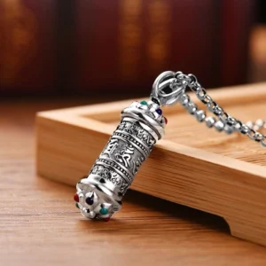 Handmade Tibetan prayer wheel pendant with Om Mani Padme Hum engraving on silver chain, top-side angle on wooden tray