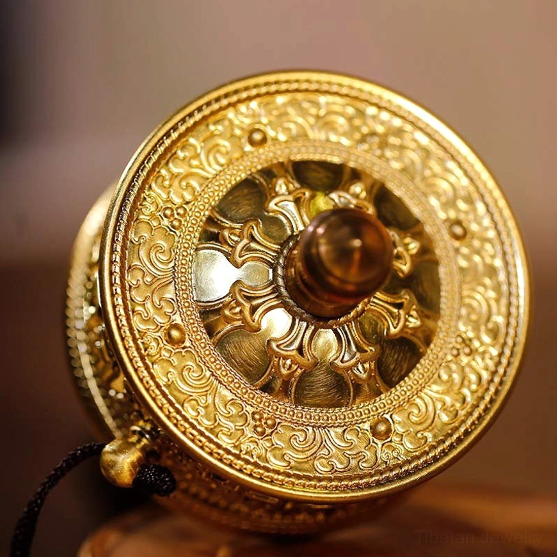 Close-up detail of Tibetan prayer wheel rear section with intricate relief carvings, polished gold metal finish, and dark brown sandalwood handle hub