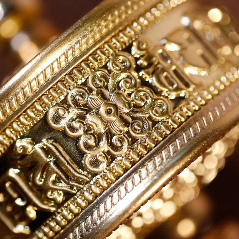 Extreme close-up side view of Tibetan prayer wheel metal surface with embossed Sanskrit scriptures, ornate decorative patterns, and polished gold finish