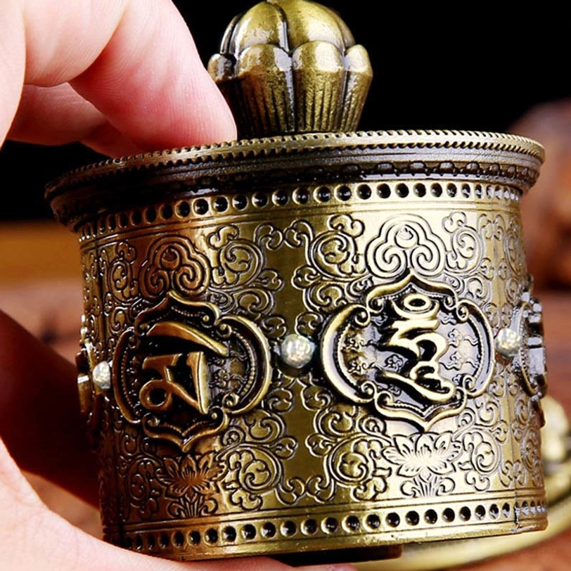Tibetan prayer wheel side close-up detail of intricate embossed patterns and riveted rim in bronze tone