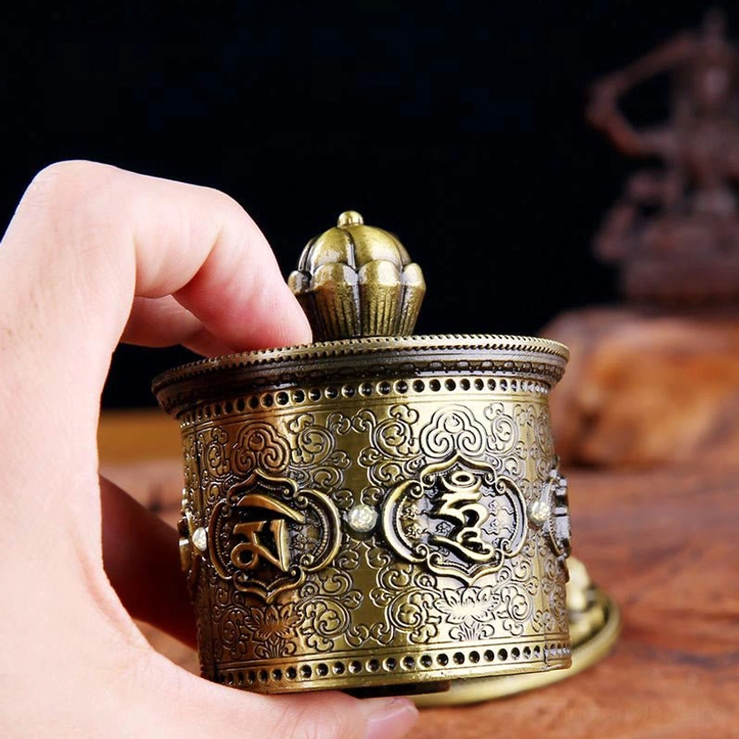 Close-up of Tibetan prayer wheel with finger adjusting top finial showing clear mantra carvings in detail