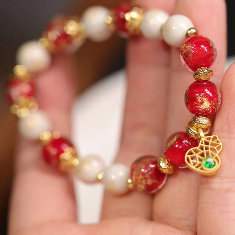 Hand-held close-up of Tibetan incense ash porcelain and liuli glass bracelet revealing gold foil details on red beads and metallic spacer hardware
