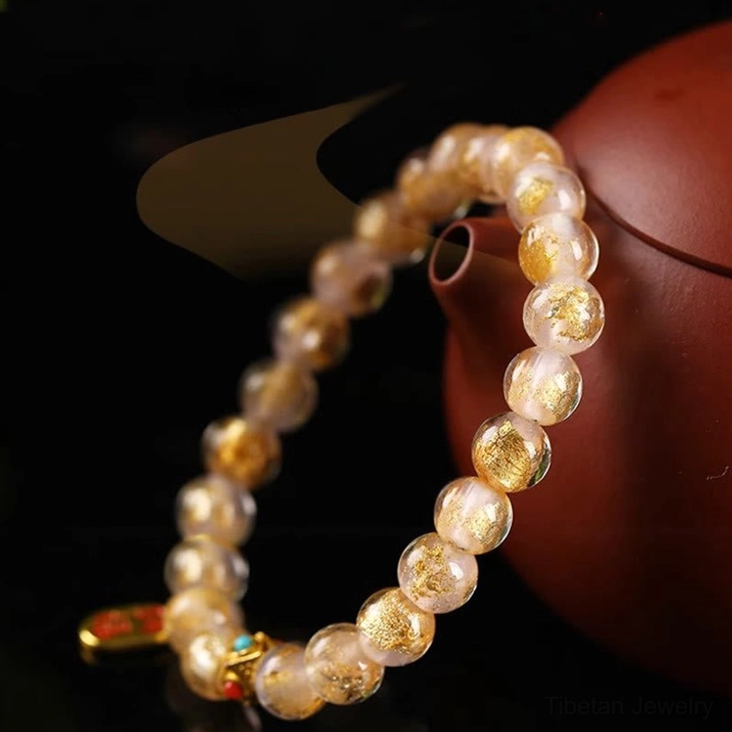 Oval translucent incense ash glass beads with gold foil and mixed metal pendants on red teaware background
