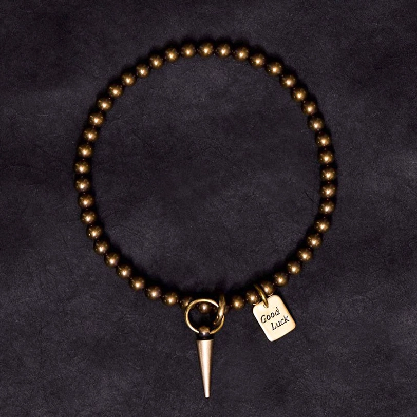Complete overhead view of handmade copper prosperity bracelet with spike charm and good luck tag on black background