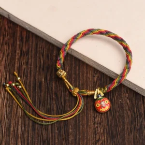 Tibetan prosperity bracelet with rainbow woven rope, gold fasteners, enamel charm, and beaded tassel on notebook