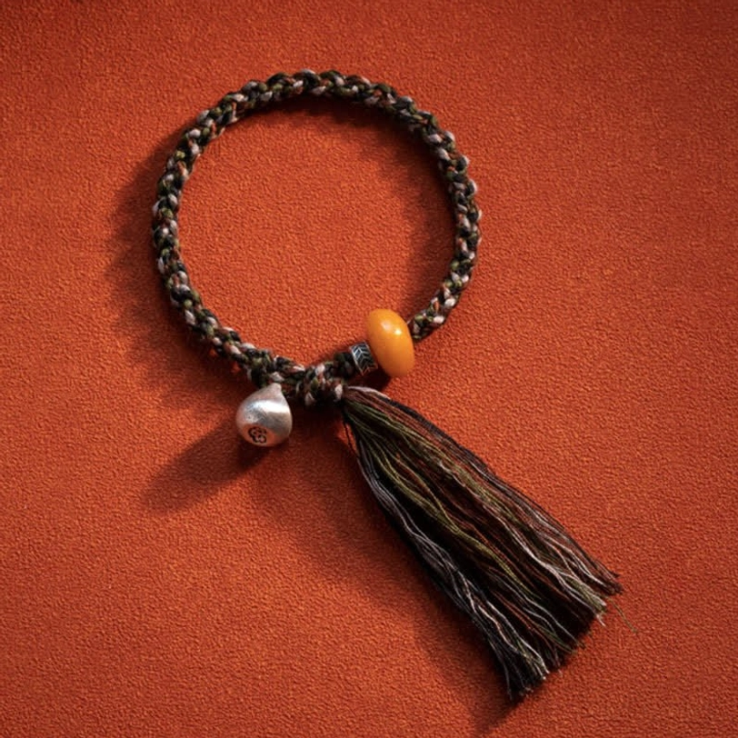 Tibetan amber steelyard protection bracelet flat lay on orange background showing complete design with multicolor woven cord, golden amber, silver charm, and tassel