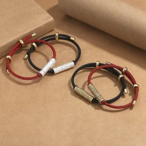 Matching Tibetan Tai Sui protection bracelets with engraved metal tubes on kraft paper background, showing red and black rope variations