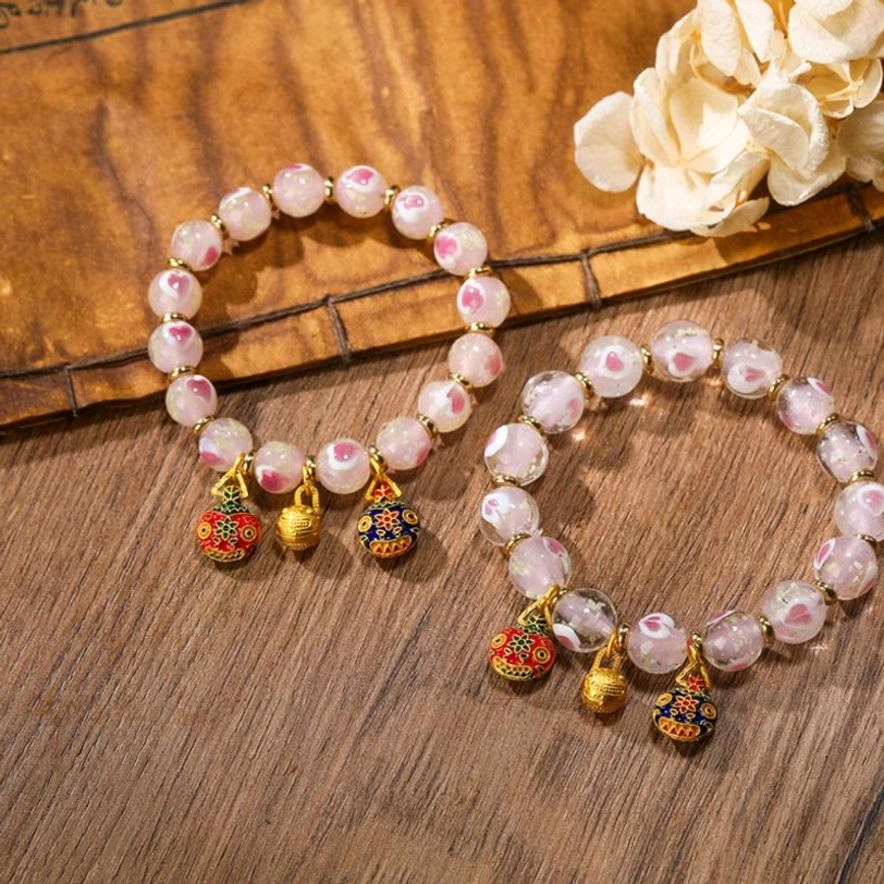 Two matching Tibetan protection bracelets with pink glass beads and enamel charms on wooden table with dried flowers