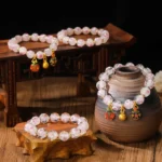 Multiple Tibetan protection bracelets with luminous pink glass beads and gold beast charms displayed on wooden furniture