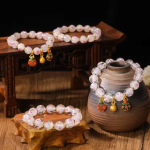 Multiple Tibetan protection bracelets with luminous pink glass beads and gold beast charms displayed on wooden furniture