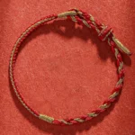 Handmade Tibetan zodiac protection bracelet with red and gold braided cord on matte fabric backdrop