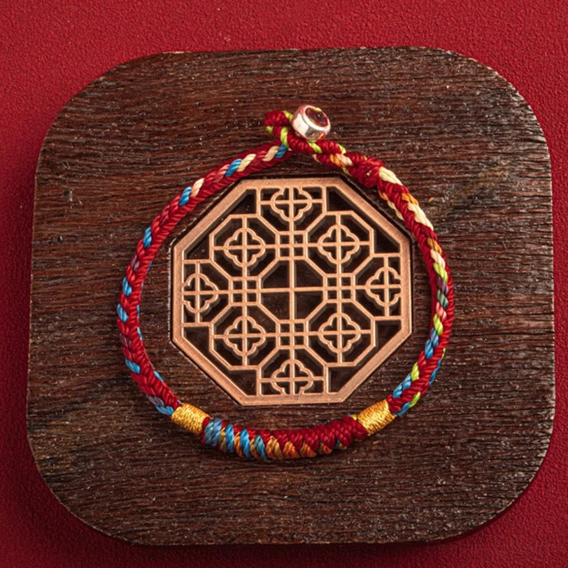 Tibetan lucky bracelet with King Kong knot placed on traditional wooden coaster, red backdrop, overhead view