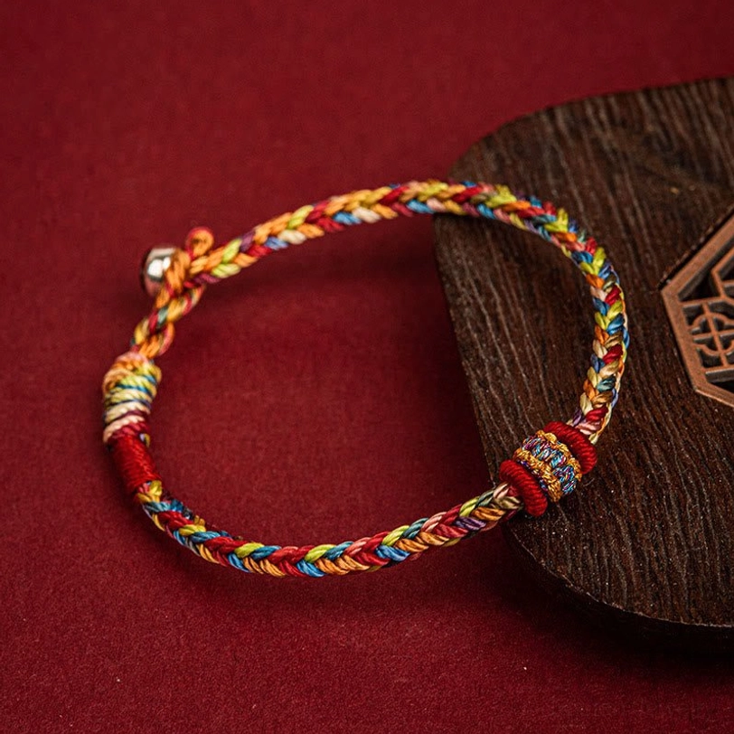 Tibetan blessing cord bracelet woven in multiple colors displayed on carved wooden coaster showing detailed braided texture and metal fastener