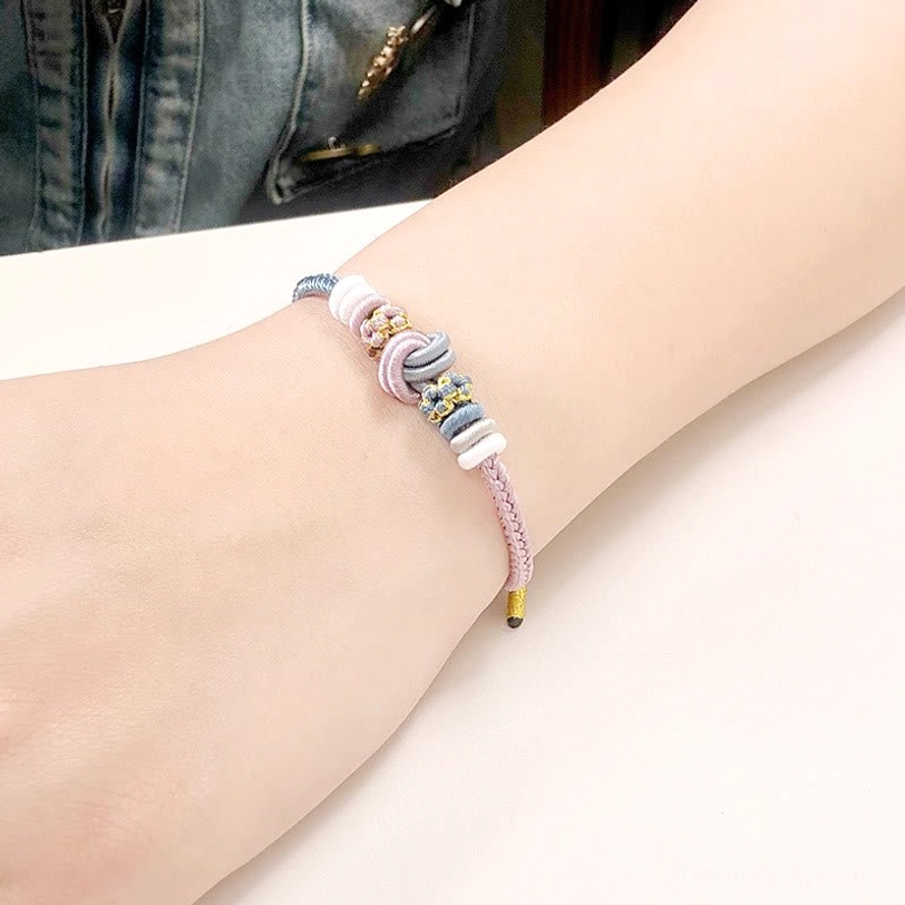 Tibetan eight-thread peace knot bracelet in soft pastel colors worn on wrist with denim, showing handwoven spiritual design