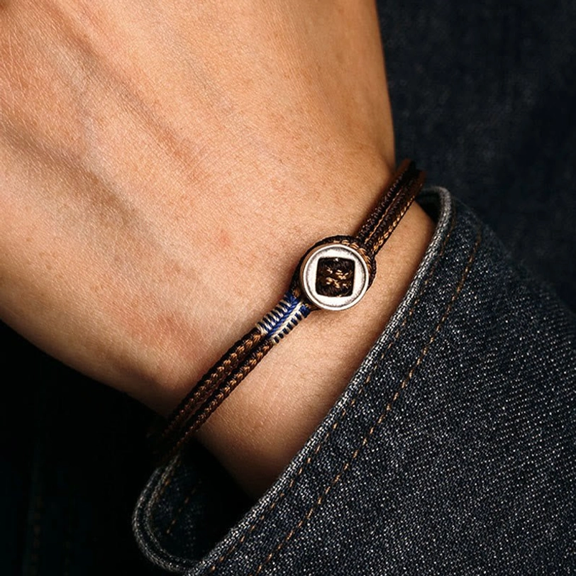 First-person view of brown and blue woven tibetan protection bracelet worn on wrist with denim sleeve, showing silver central buckle fit