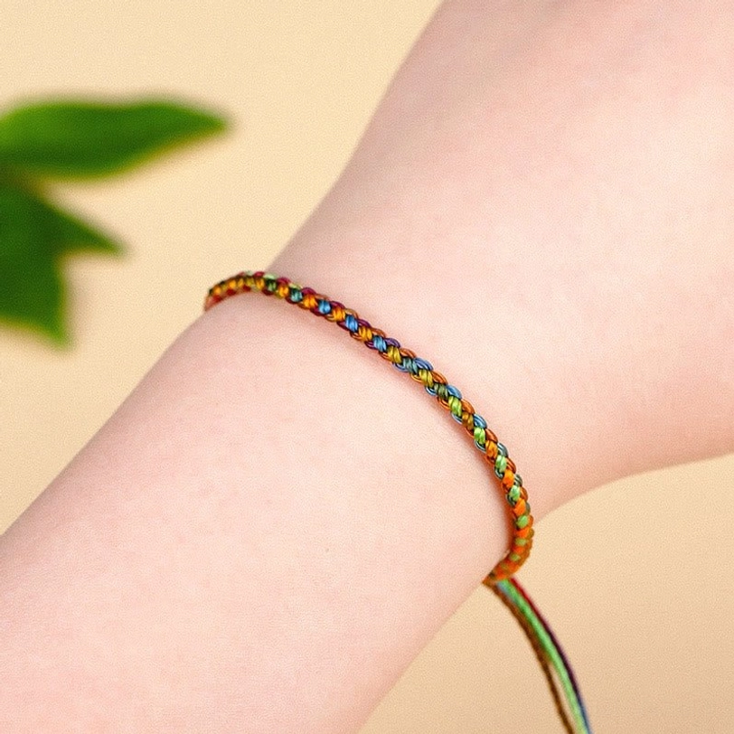 Multicolored Tibetan luck bracelet worn on wrist with adjustable long tail end and green leaf decoration