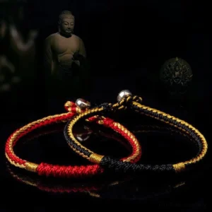 Two Tibetan handmade braided bracelets in red-gold and black-gold, top-down view with Buddha statue background