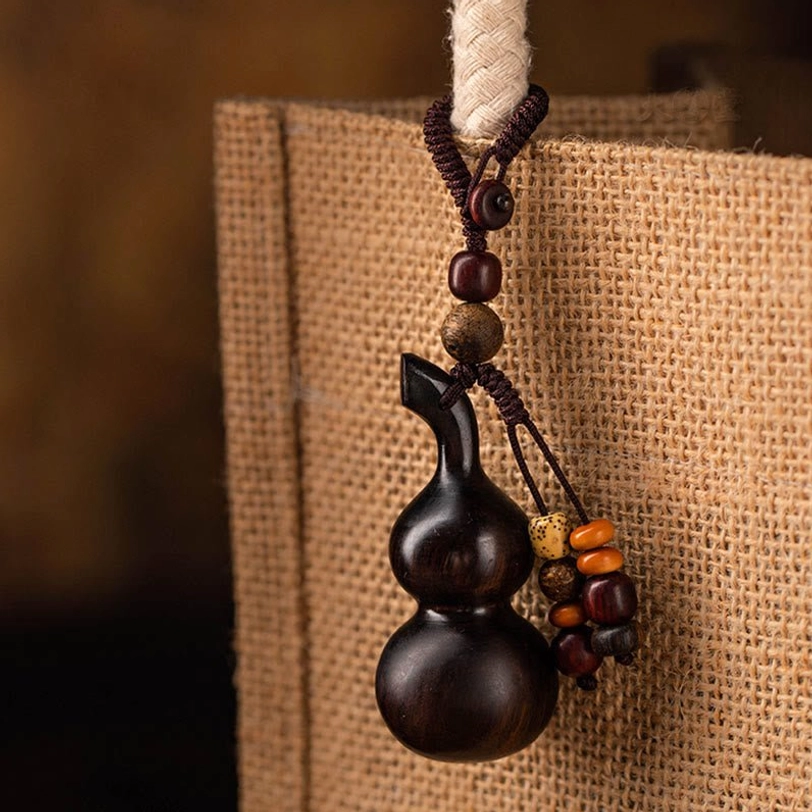 Deep brown wooden gourd keychain with mixed bead tassel hung on burlap tote bag, close-up hanging angle demonstrating portable daily spiritual charm use