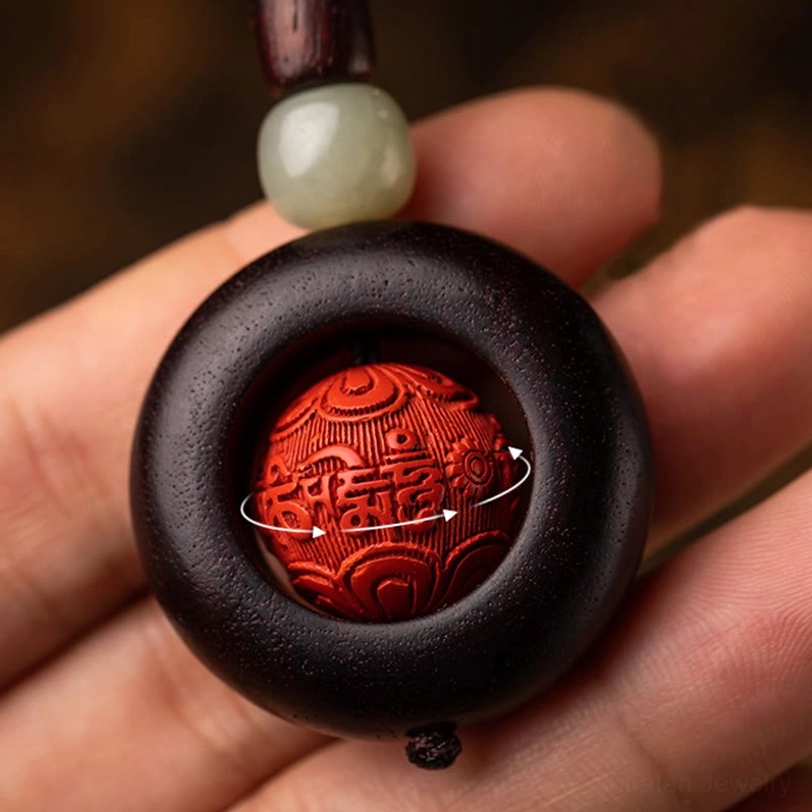 Hand holding Tibetan Om Mani Padme Hum keychain showing rotatable carved cinnabar bead and jade accents