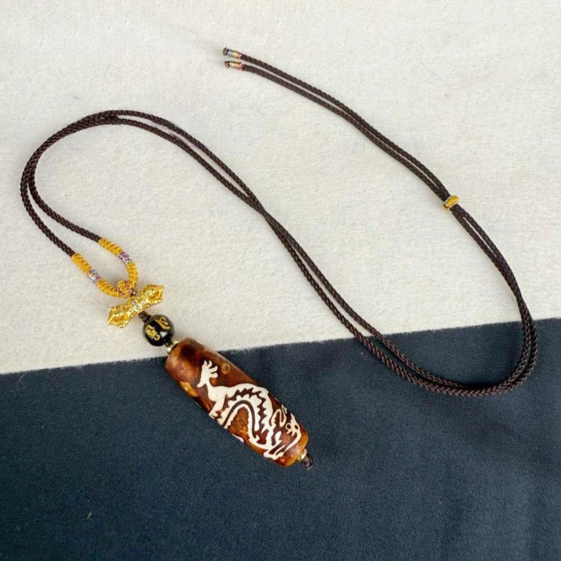 Full length display of dragon-patterned nine-eye dzi bead necklace with adjustable braided rope and decorative accents