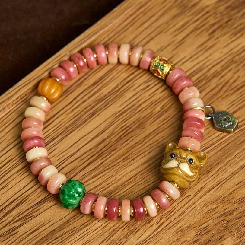 Handcrafted Tibetan protection bracelet featuring mixed pink and beige camel bone beads with green stone and pug ornament on wooden table