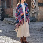 Tibetan rainbow knit shawl with geometric stripe pattern and tassels worn as full-body wrap on ancient cobblestone street
