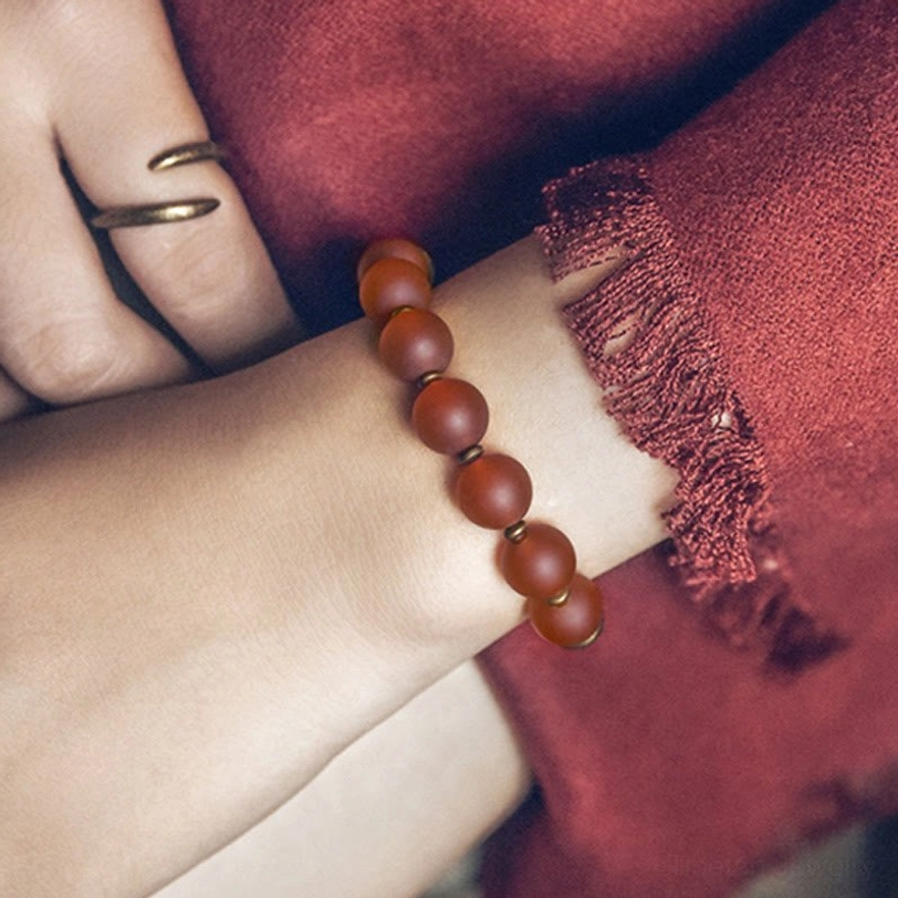 Red agate beaded bracelet on wrist displaying matte texture and copper metal spacer beads