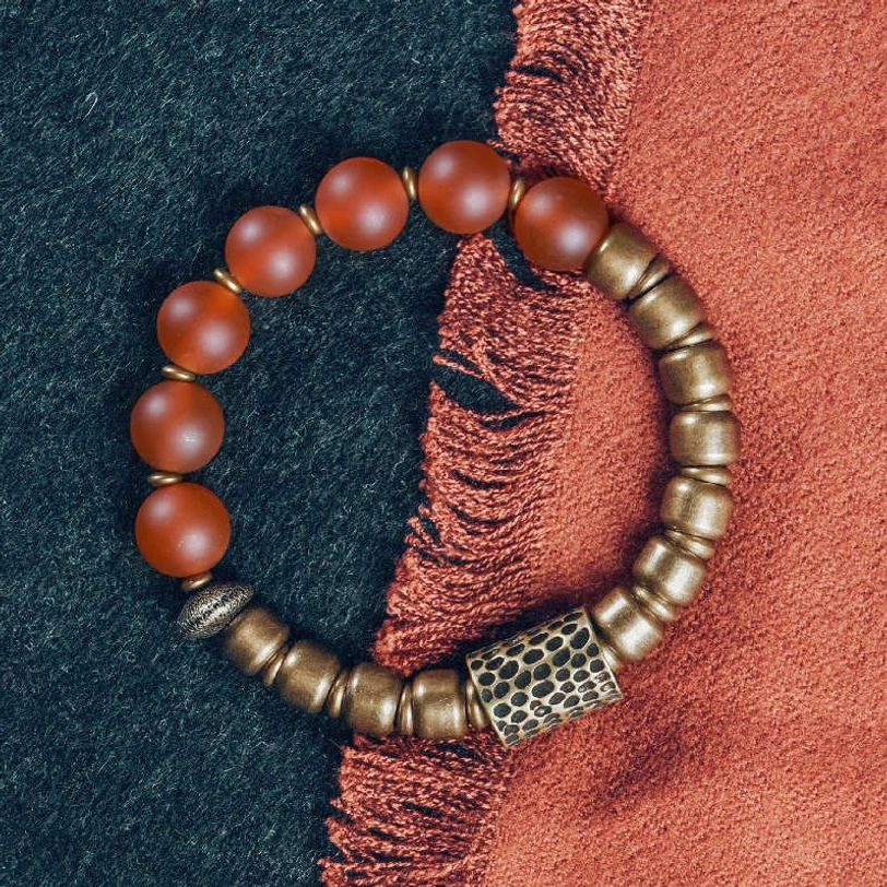 Red agate and antiqued copper beaded bracelet with matte reddish-brown stones and engraved barrel charm in flat lay
