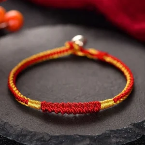 Handmade Tibetan red and gold braided protection bracelet with silver clasp, displayed on dark stone surface with spiritual ornament