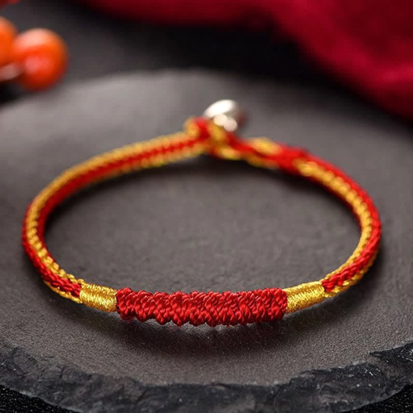 Handmade Tibetan red and gold braided protection bracelet with silver clasp, displayed on dark stone surface with spiritual ornament