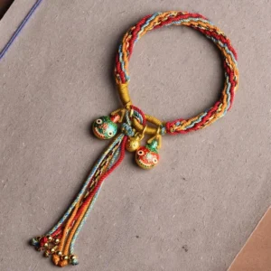 Red and gold Tibetan reincarnation knot bracelet with enamel beast pendant and long tassel on grey background