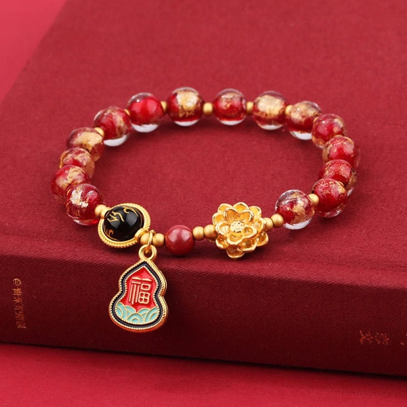 Red and gold Tibetan Liuli glass spiritual bracelet with lotus charm and enamel Fu pendant on red book surface