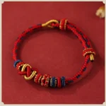 Red tibetan peace knot blessing bracelet with gold accents and braided sacred knot design, flat lay top view