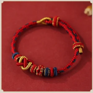 Red tibetan peace knot blessing bracelet with gold accents and braided sacred knot design, flat lay top view