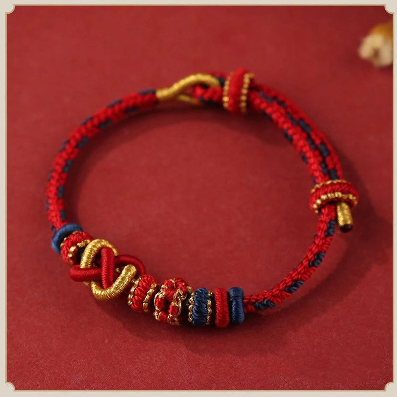 Red tibetan peace knot blessing bracelet with gold accents and braided sacred knot design, flat lay top view