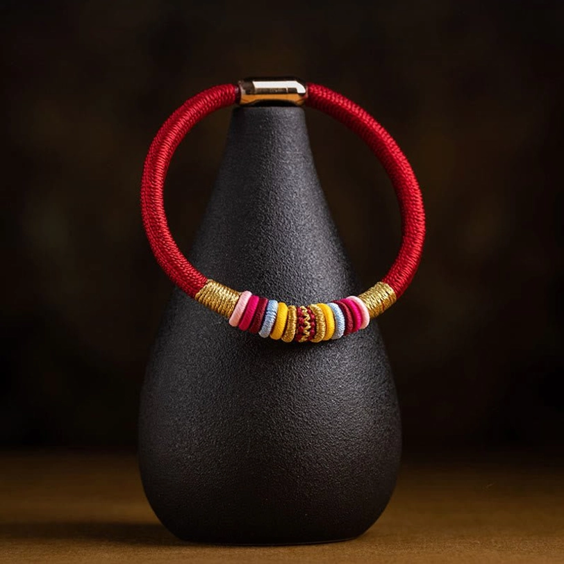Red braided Tibetan Vajra Knot protection bracelet with colorful wrapped bands, ceramic stand display