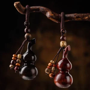 Two handcrafted gourd keychains in red sandalwood and ebony wood hung on wooden branch, side view showcasing different bead tassel styles and mixed wood colors
